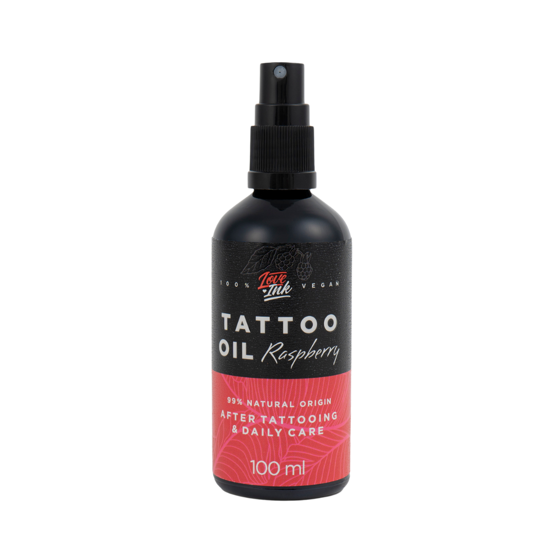 Na zdjęciu znajduje się butelka oleju do tatuaży o zapachu malinowym od marki Love Ink. Butelka jest czarna z różową etykietą i napisem "Tattoo Oil Raspberry". Etykieta informuje, że olej jest w 99% pochodzenia naturalnego i przeznaczony do pielęgnacji po tatuażu oraz do codziennego użytku. Pojemność butelki wynosi 100 ml. Design jest prosty i nowoczesny, podkreślający naturalny i wegański charakter produktu.