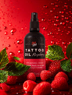 Na zdjęciu znajduje się butelka oleju do tatuaży o zapachu malinowym od marki Love Ink. Butelka jest czarna z różową etykietą i napisem "Tattoo Oil Raspberry". Wokół butelki znajdują się świeże maliny i zielone liście na czerwonym tle z kroplami wody, co dodaje świeżości i naturalności. Olej jest oznaczony jako 100% naturalny i wegański, przeznaczony do codziennej pielęgnacji po tatuażu.