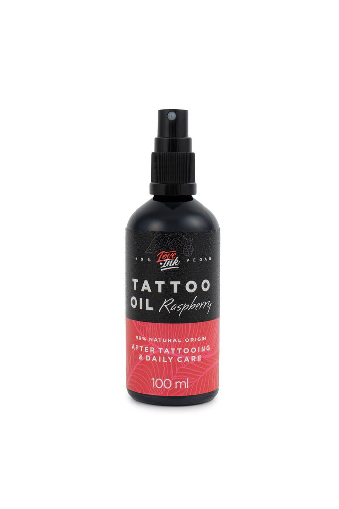 Na zdjęciu znajduje się butelka oleju do tatuaży o zapachu malinowym od marki Love Ink. Butelka jest czarna z różową etykietą i napisem "Tattoo Oil Raspberry". Etykieta informuje, że olej jest w 99% pochodzenia naturalnego i przeznaczony do pielęgnacji po tatuażu oraz do codziennego użytku. Pojemność butelki wynosi 100 ml. Design jest prosty i nowoczesny, podkreślający naturalny i wegański charakter produktu.
